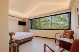 Spacious hotel room with large window overlooking lush green mountains.