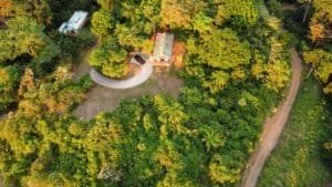 Aerial view of a house surrounded by lush green forest and winding dirt roads.