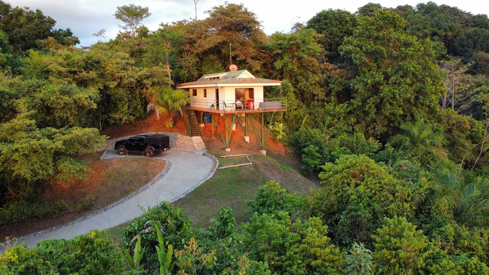 Elevated house with ocean and mountain views surrounded by lush greenery.