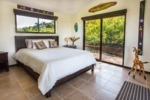 Bedroom with large window and balcony overlooking lush greenery in Dominical.