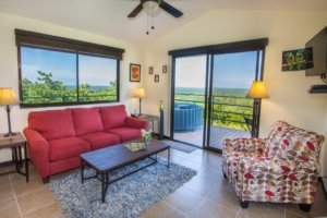 Living room with ocean view, red sofa, patterned armchair, and balcony.