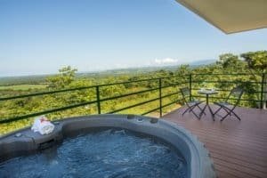 Balcony with hot tub, outdoor table, and scenic ocean and mountain view.