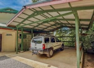 Covered carport with SUV and green support beams in Dominical estate.
