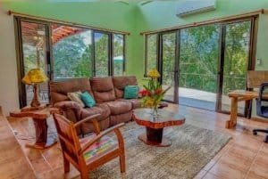 Bright living room with large windows, wooden furniture, and tropical views.