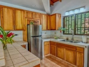 Bright kitchen with wooden cabinets, stainless steel fridge, and large window.
