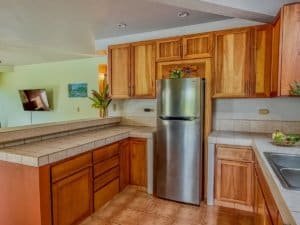Warm kitchen with wooden cabinets, stainless steel fridge, and tiled countertops.