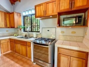 Kitchen with wooden cabinets, stove, microwave, and window in Dominical area.