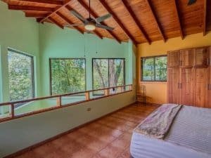 Bright bedroom with large windows, wooden ceiling, and a bed with a blanket.