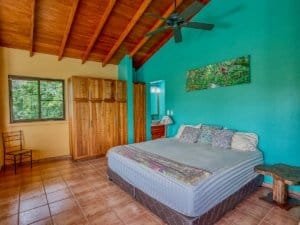 Bright bedroom with wooden ceiling, colorful wall art, and large window.