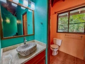Interior view of a bathroom with a stone sink, colorful walls, and a window showing greenery.