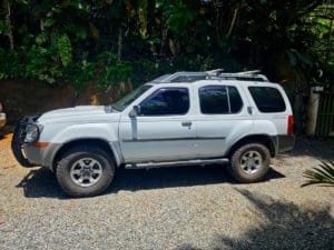 White 4x4 SUV parked on gravel with lush greenery background.