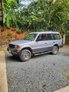Silver SUV parked on gravel with lush tropical background in Dominical.