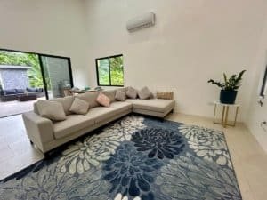 Spacious living room with beige sofa, tropical decor, and large windows.