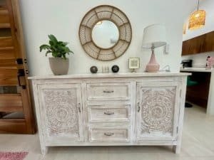 Elegant white wooden sideboard with mirror, plant, and decor in tropical home.
