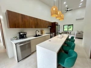 Contemporary kitchen with white countertops, wooden cabinets, and green bar stools.