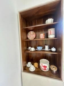 Wooden shelf with colorful ceramic dishes and cups for home decor.