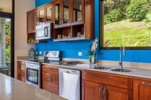 Kitchen with wooden cabinets, blue wall, and view of greenery outside.