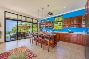 Bright kitchen with blue walls, wooden cabinets, and ocean view in Dominical.