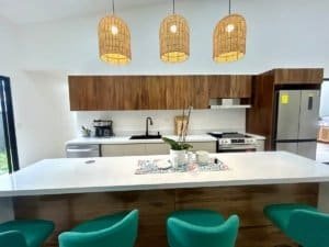 Contemporary kitchen with wooden cabinets, white countertops, and green chairs.