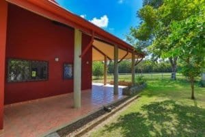 Red Hacienda style home with porch, surrounded by green trees and lawn in Costa Rica.
