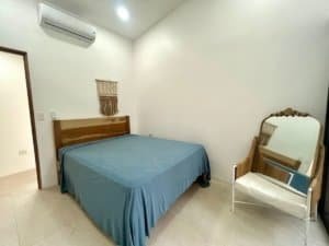 Clean bedroom with blue bedspread, mirror, and air conditioner in Dominical.