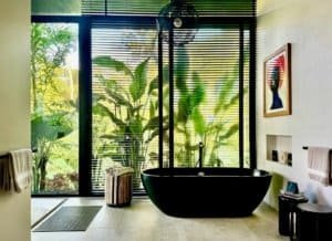 Modern bathroom with black bathtub and large windows overlooking lush greenery.