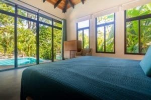 Bedroom with ocean view, large windows, tropical greenery, and pool view.