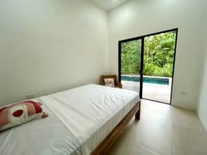 Bedroom with sliding glass door opening to lush tropical garden and pool.