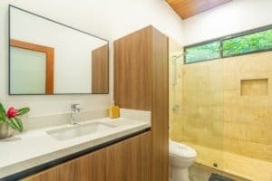 Bright bathroom with wooden cabinets, large mirror, and walk-in shower with window.