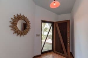 Interior view of a home entry with wooden door, mirror, and natural light.
