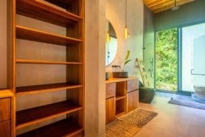 Interior of Japanese-style home with wooden shelves and large glass doors to jungle.