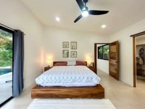 Bright bedroom with wooden bed, ceiling fan, and sliding glass door to pool area.