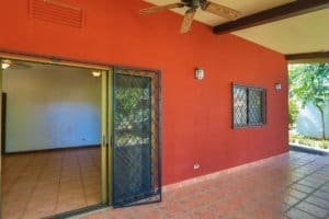 Covered patio with red wall, ceiling fan, and garden view in Dominical.