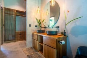 Contemporary bathroom with wooden vanity, round mirror, and hanging lights.