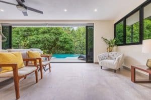 Bright living room with large glass doors opening to pool and rainforest.