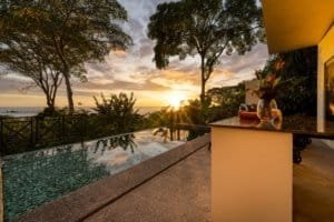 Sunset view from a villa with pool overlooking ocean and tropical trees.