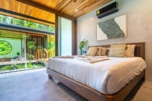 Cozy bedroom with large glass doors overlooking lush jungle in Costa Rica.