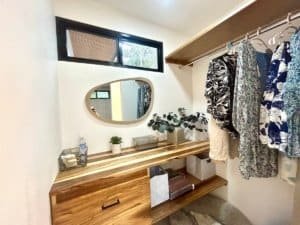 Interior view of a tropical home closet with clothes, mirror, and wooden shelf.