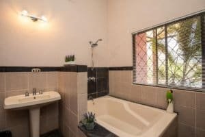 Bathroom with bathtub, sink, and window overlooking greenery.