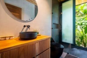 Contemporary bathroom with black sink and lush jungle view through glass door.