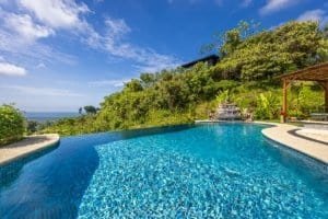 Infinity pool with ocean view, lush garden, and outdoor seating area in Dominical.