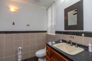Bathroom with beige tiles, window blinds, and a mirror above the sink.