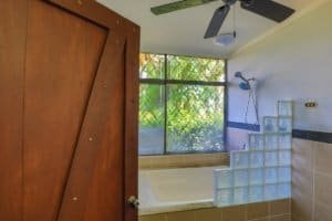 Bathroom with large window, glass block wall, and ceiling fan in a Costa Rican home.