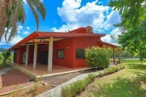 Red Hacienda-style home with lush garden and palm trees in Dominical.