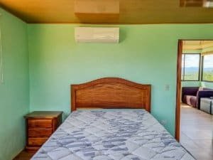 Bedroom with wooden bed, green walls, and mountain view through window.