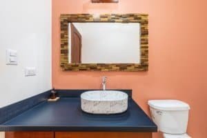 Modern bathroom with marble sink, wooden mirror frame, and coral wall.