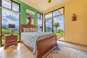 Bright bedroom with large windows overlooking lush tropical landscape and ocean.