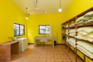 Bright yellow laundry room with washing machine, sink, and shelves for linens.