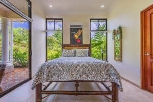 Bright bedroom with large windows overlooking lush garden and outdoor patio.