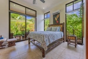 Bright bedroom with large windows overlooking lush tropical garden in Dominical.